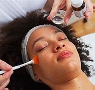Woman receiving a facial treatment. A professional applies a product to her face, while a bottle sits nearby.