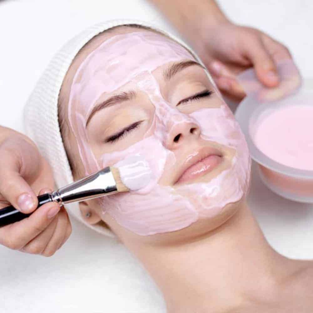 Person getting a facial treatment with gloved hands, eyes closed, white headband.