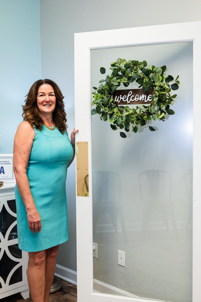 A woman in a blue dress is standing in front of a door with a wreath on it.