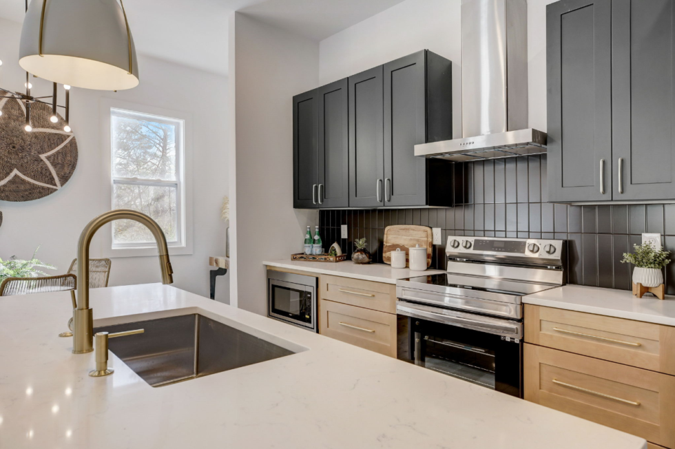 Modern kitchen with gray cabinets, white island countertop, gold faucet, and stainless steel appliances