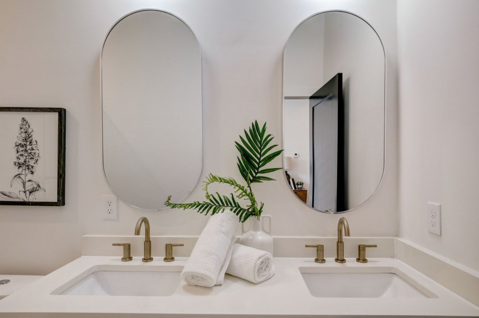 Modern double bathroom vanity with oval mirrors, brass faucets, and rolled white towels
