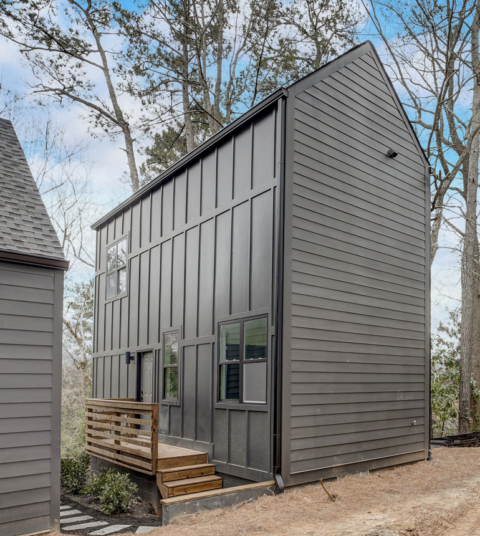 Modern gray tiny house with a steep roof, front porch, and trees in the background