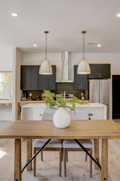 Bright kitchen-dining area with wood table, white vase, pendant lights, and dark cabinets