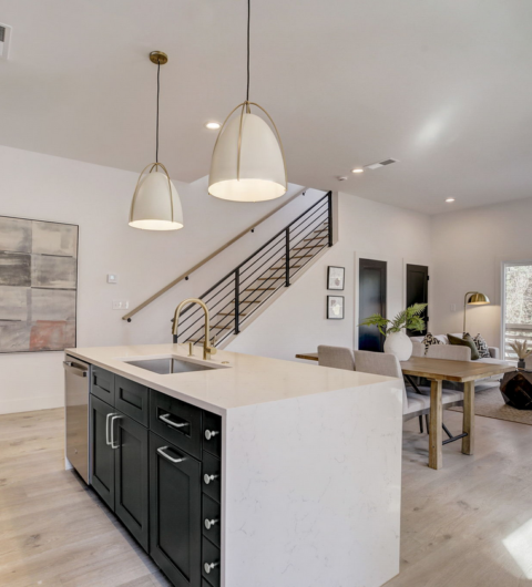 Modern open-plan kitchen and dining area with white island, pendant lights, staircase, and light wood flooring