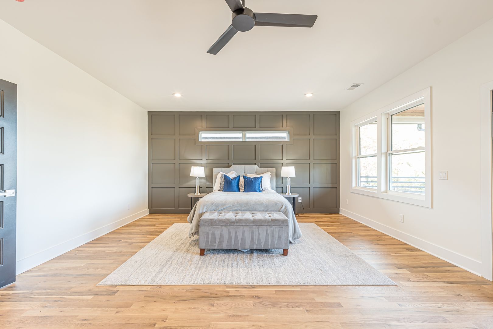 Modern bedroom with a bed, wood floors, gray accent wall, and large windows