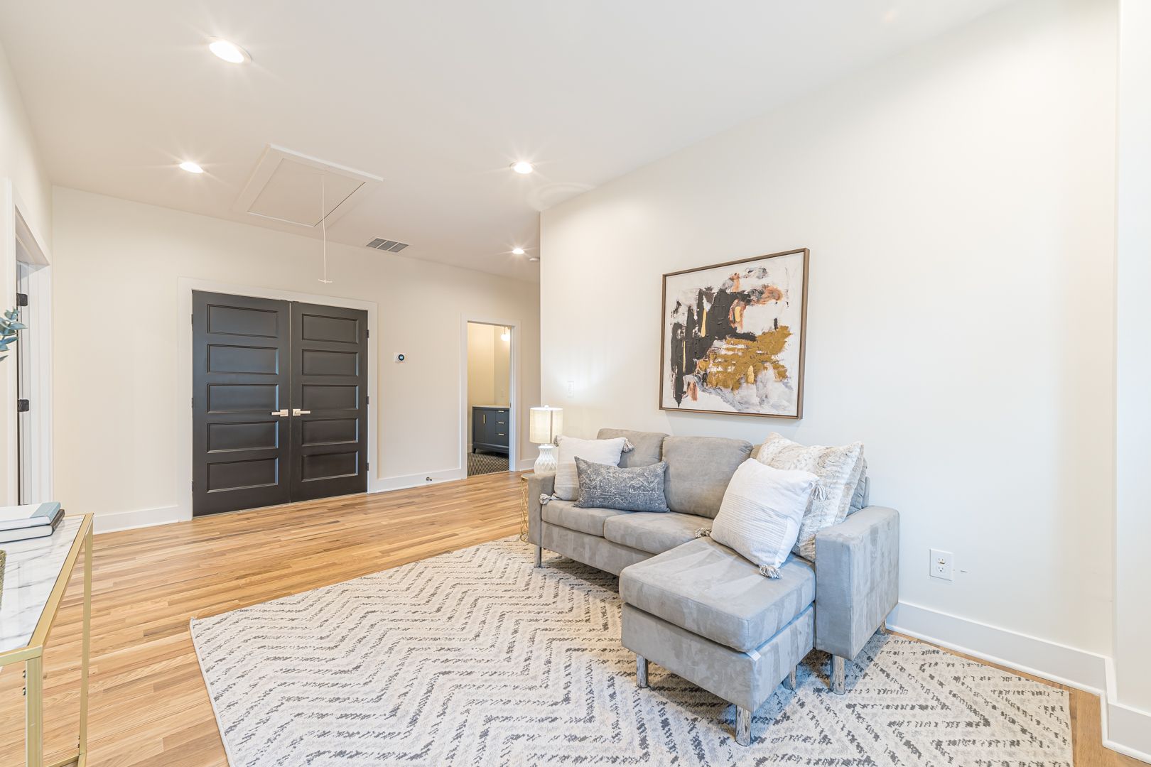 Bright living room with gray sectional, patterned rug, dark double doors, and abstract wall art.