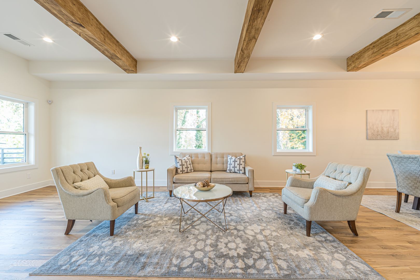 Bright living room with beige seating, patterned rug, exposed wood beams, and large windows