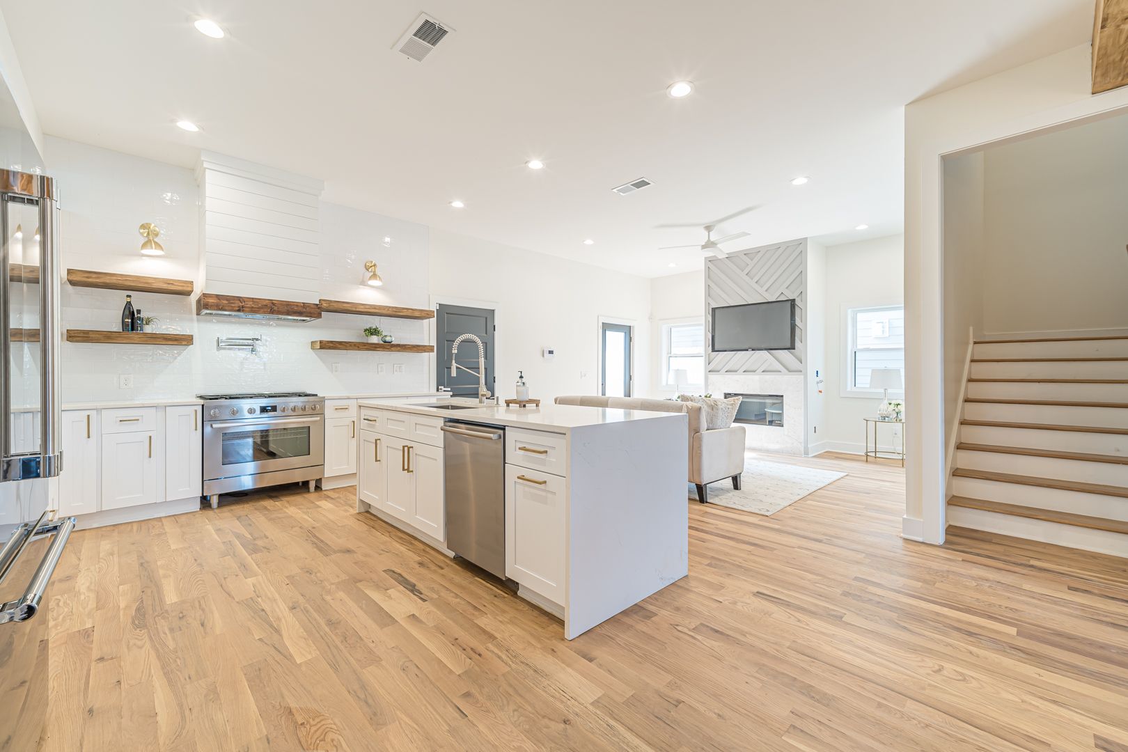 Bright open-plan kitchen and living area with white cabinets, wood floors, and a staircase on the right