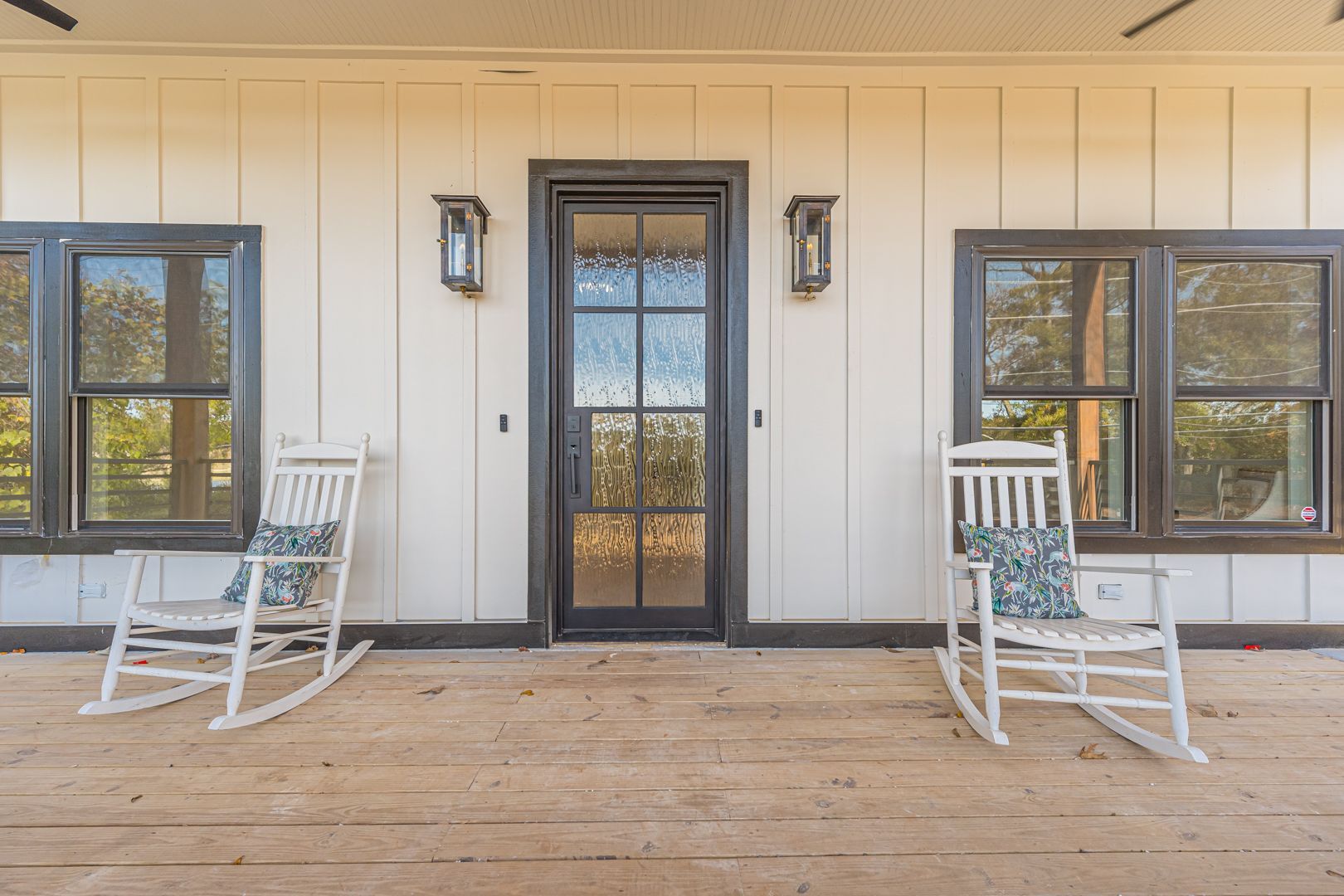 Front porch with white rocking chairs, black-framed glass door, and matching windows on a cream exterior.