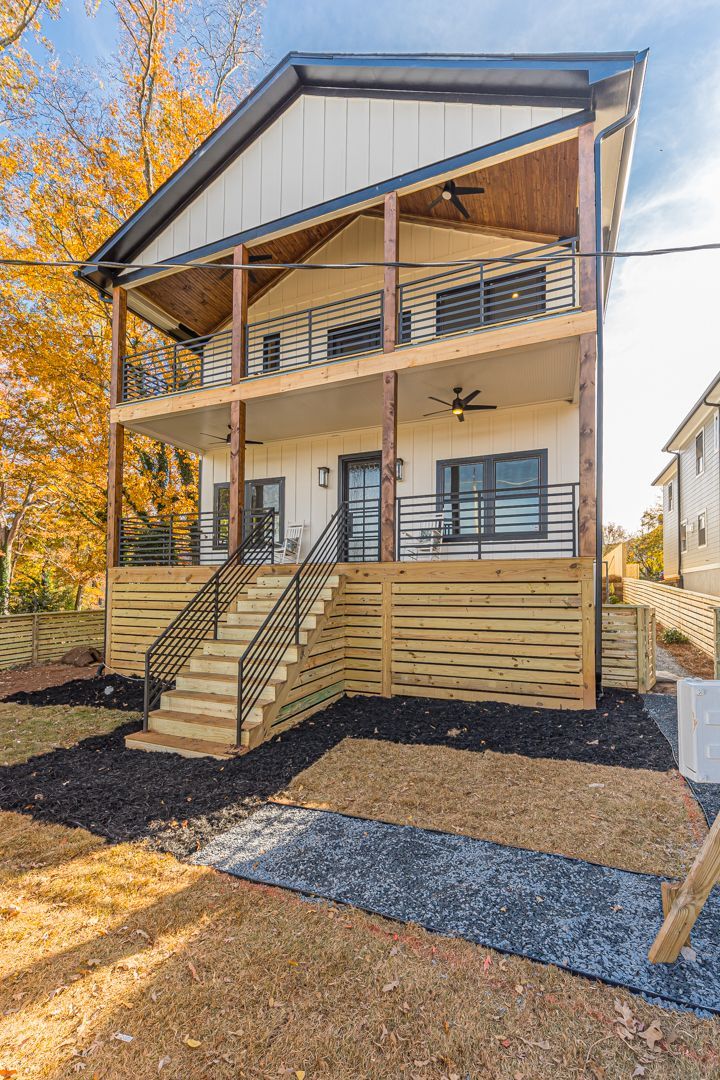 Two-story modern house with wooden deck, exterior stairs, and covered porch in a wooded yard.
