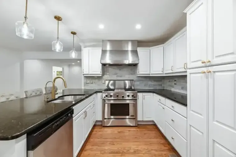 Modern white kitchen with stainless steel appliances, dark countertops, and pendant lights