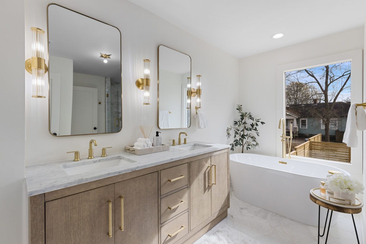 Bright modern bathroom with double vanity, gold fixtures, and large soaking tub by a window