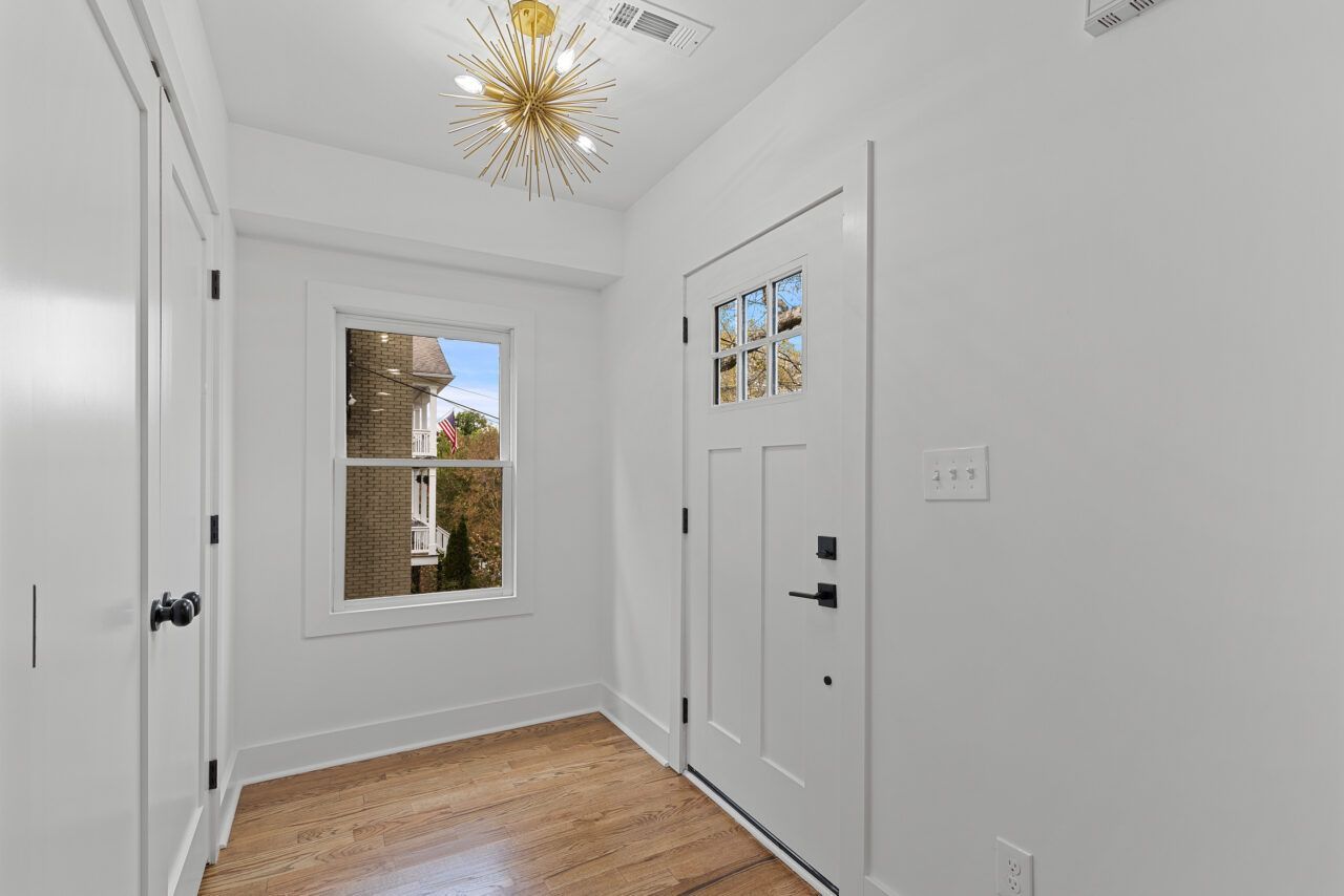 Bright white entry hallway with wood floor, front door, window, and gold ceiling light.
