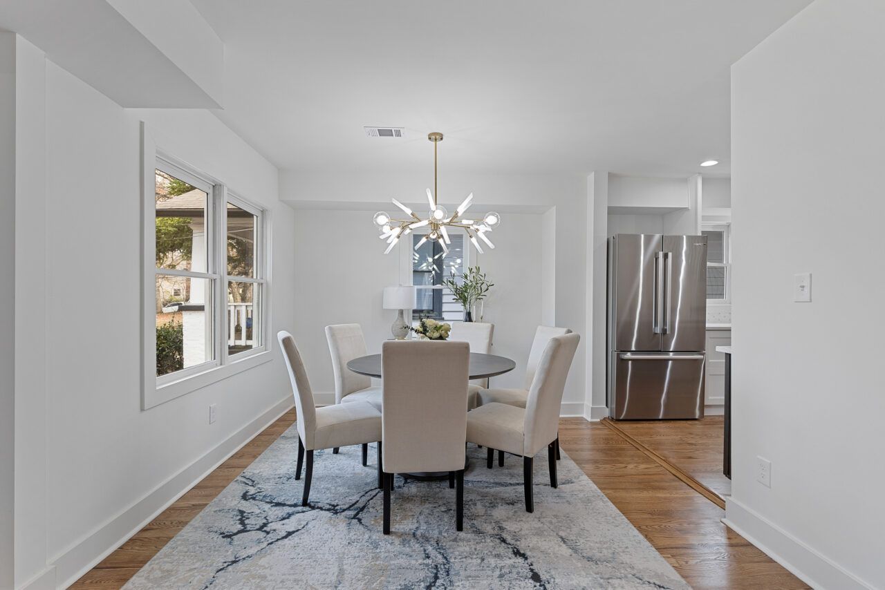 Bright dining room with a white table, upholstered chairs, rug, and stainless-steel refrigerator in the background