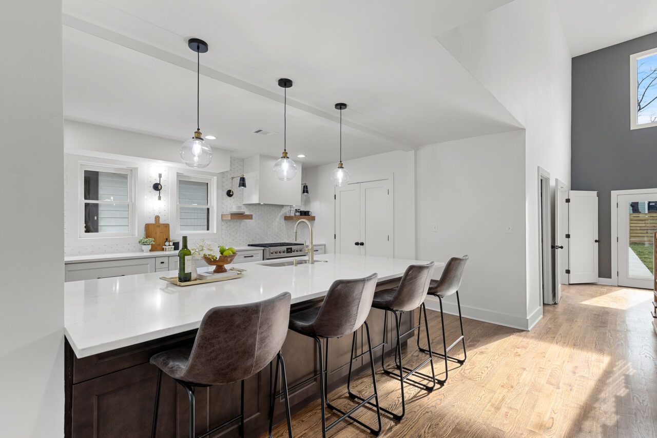 Bright modern kitchen with white island, dark bar stools, and sunlit hardwood floors