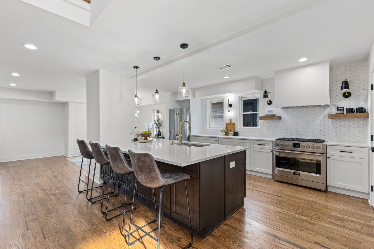 Modern white kitchen with dark island, bar stools, and stainless steel appliances