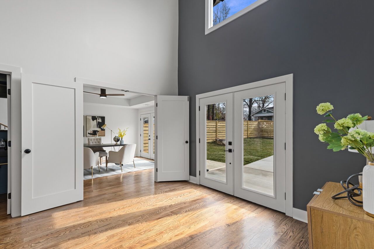 Bright modern room with open white doors, gray accent wall, hardwood floor, and a view of the yard through glass doors