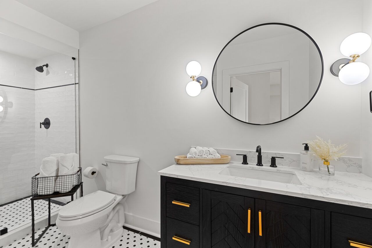 Modern bathroom with black vanity, round mirror, white marble countertop, and glass shower
