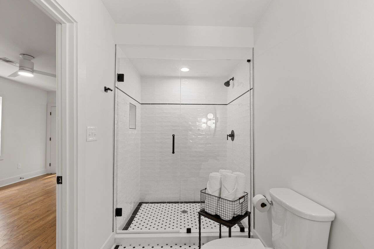 Modern white-tiled bathroom with a glass walk-in shower and toilet