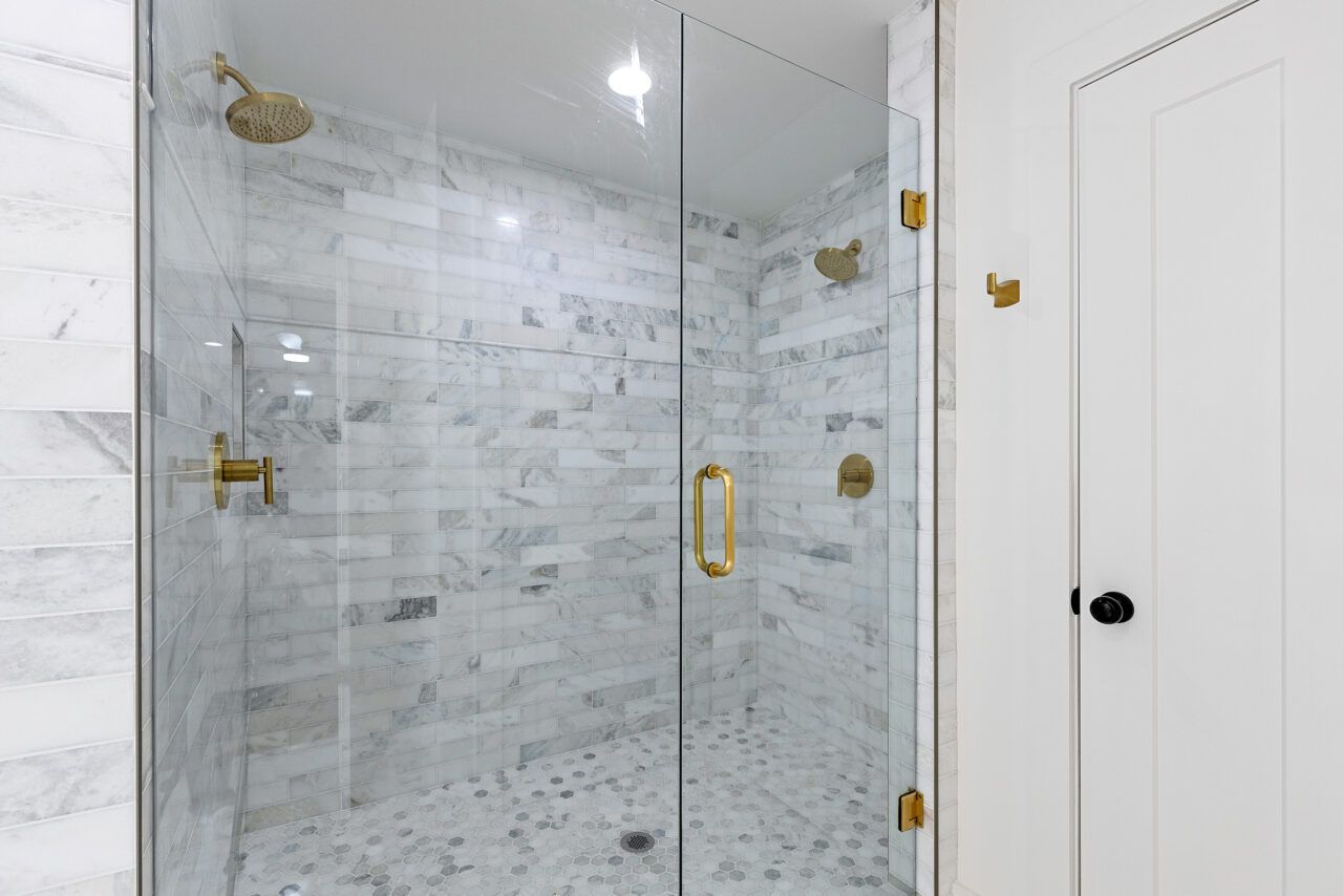 Modern bathroom shower with clear glass doors, marble tile, and gold fixtures next to a white closet door