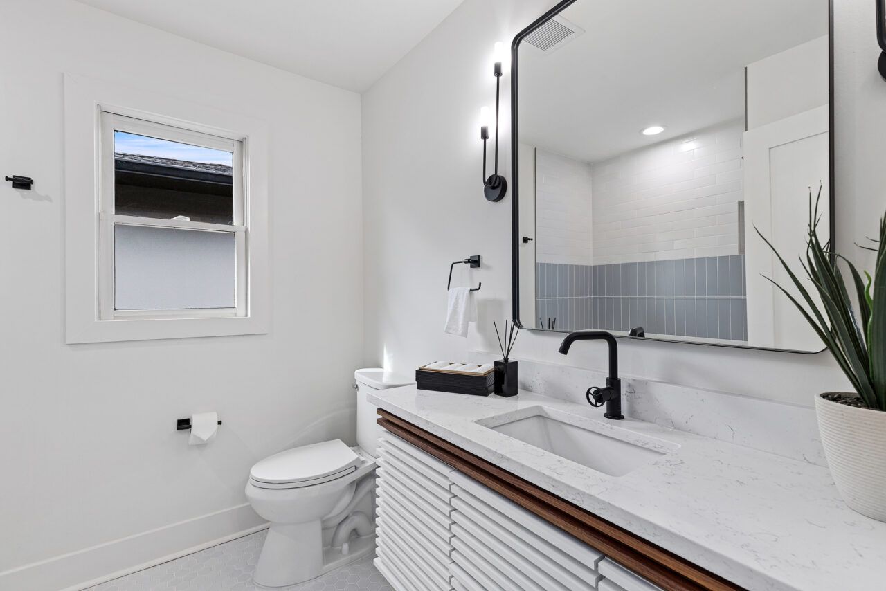 Bright white bathroom with toilet, sink, mirror, and small window, shown in a clean modern style.