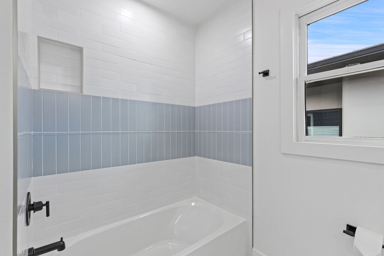 Small bathroom with a white bathtub, light blue tile accent, and window above the tub.