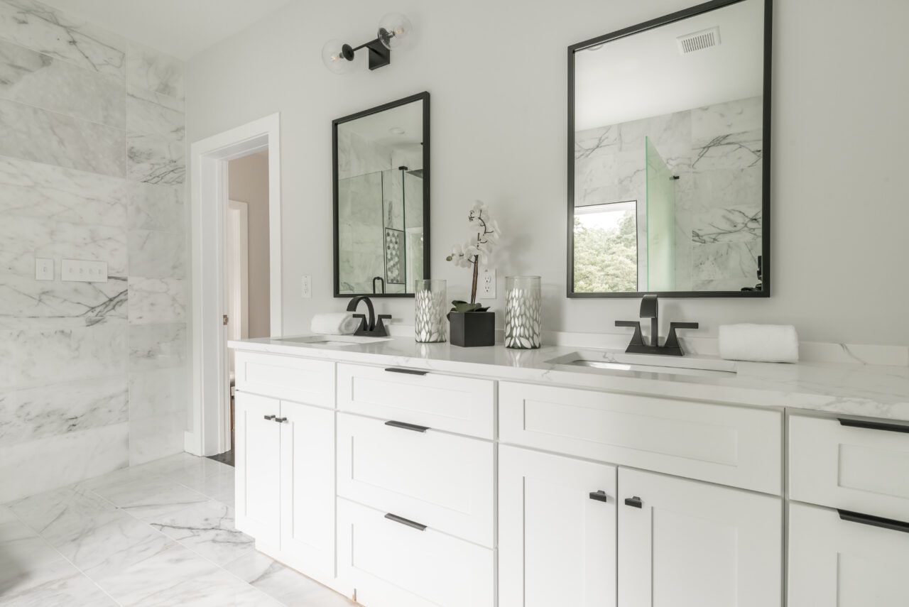Bright modern bathroom with white marble walls, double vanity, and large mirrors