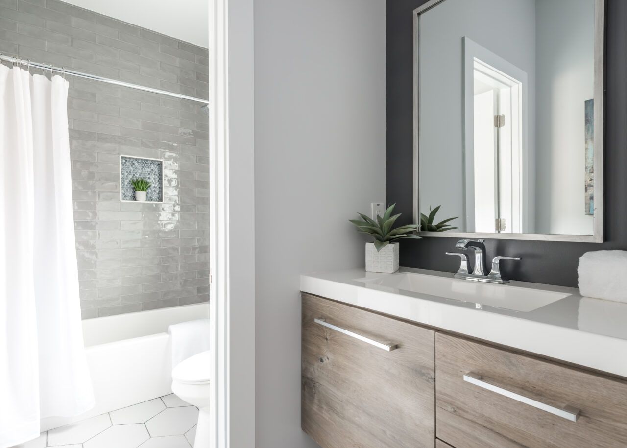 Modern bathroom vanity with mirror, sink, wood cabinets, and a glimpse of a tiled shower.
