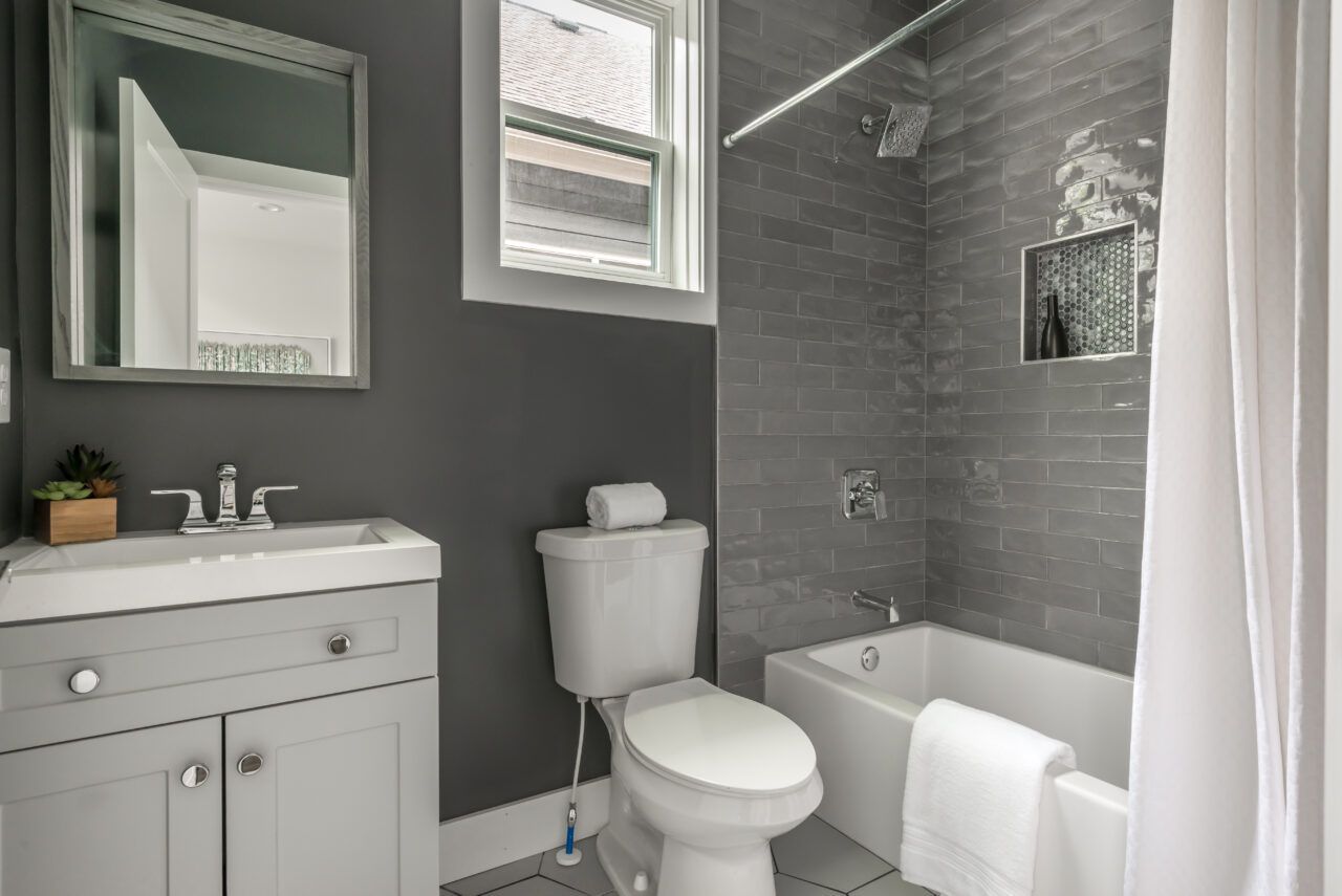 Small gray-and-white bathroom with vanity, toilet, mirror, and a bathtub with a shower curtain