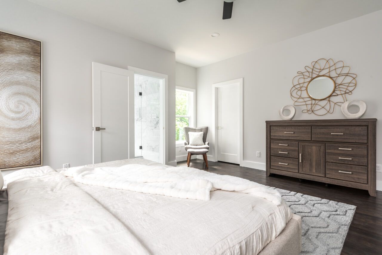 Bright bedroom with a white bed, dark wood dresser, and open doors in soft natural light