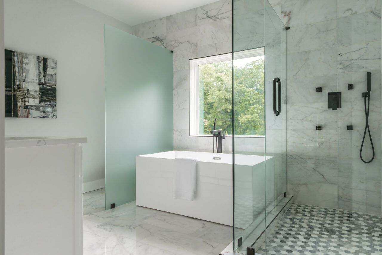 Modern white bathroom with freestanding tub, glass shower, and large window