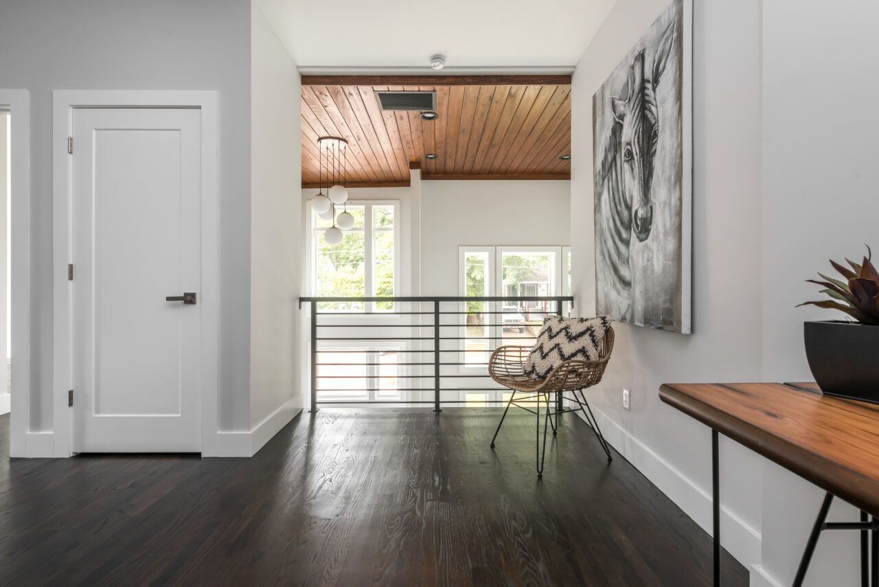 Modern hallway with dark wood floor, white walls, large lion artwork, and a wooden table by a railing.