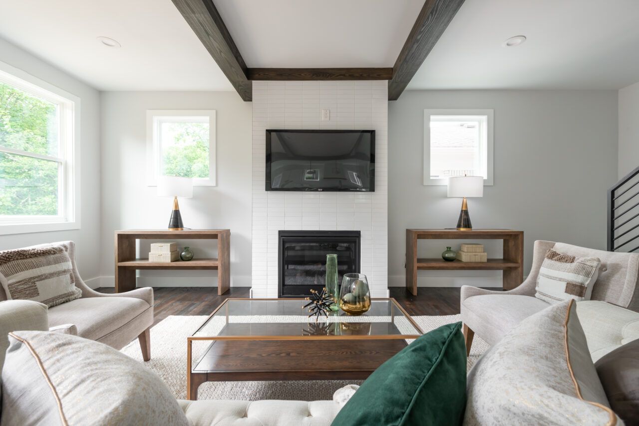 Bright, symmetrical living room with white sofas, wood coffee table, fireplace, TV, and exposed ceiling beams.