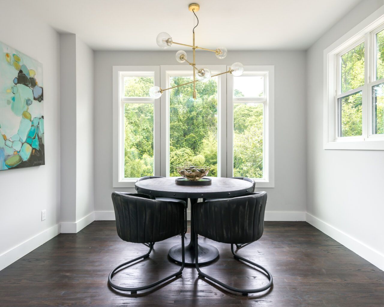 Modern dining room with round black table, four chairs, and large windows overlooking greenery