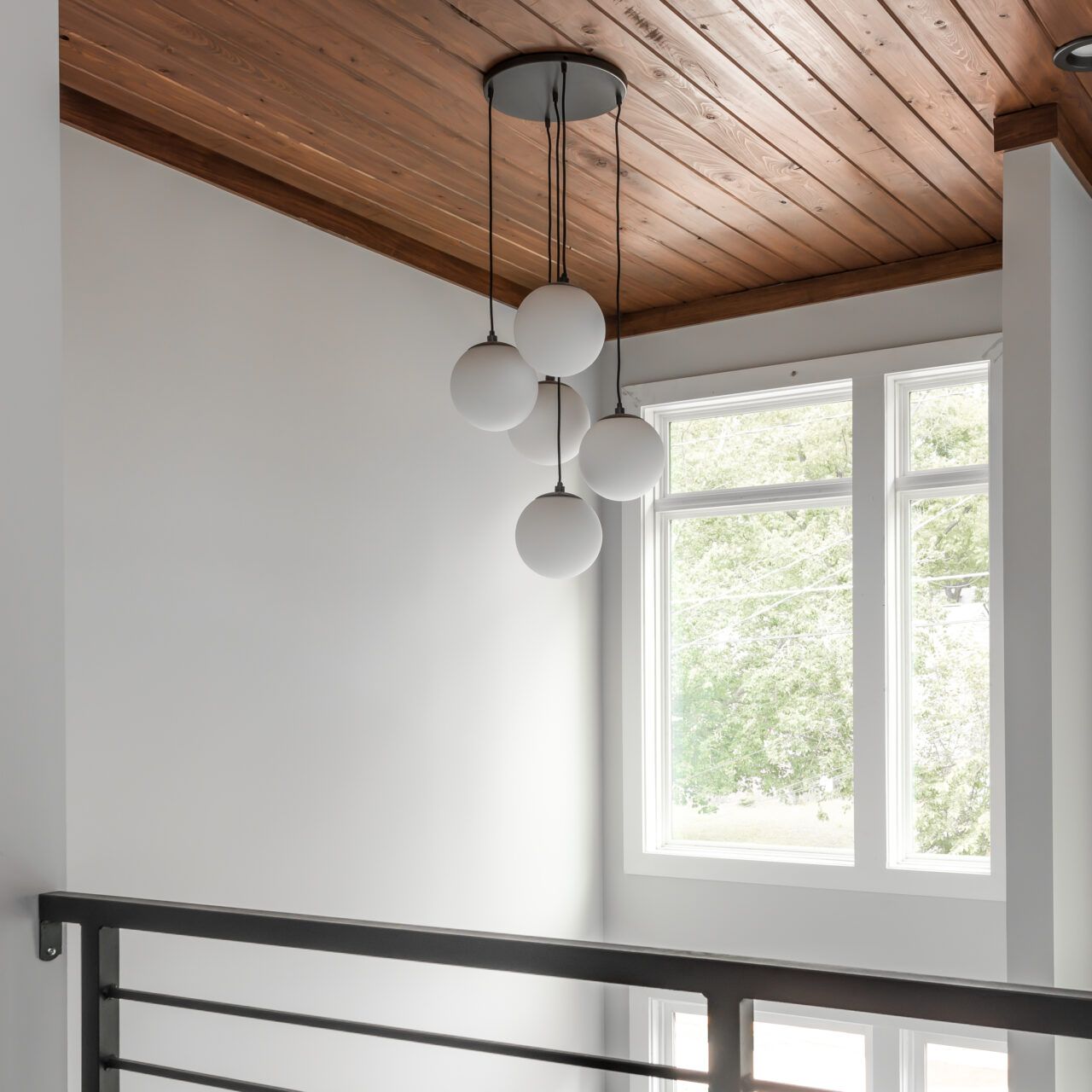 Modern stairwell with white walls, wood ceiling, hanging globe light, and a bright window.