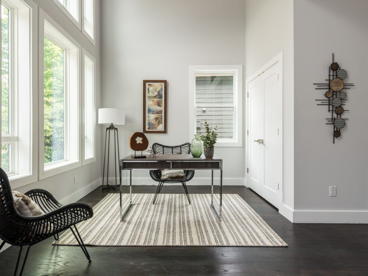 Bright home office with black desk, woven chair, large windows, and rug on dark hardwood floor