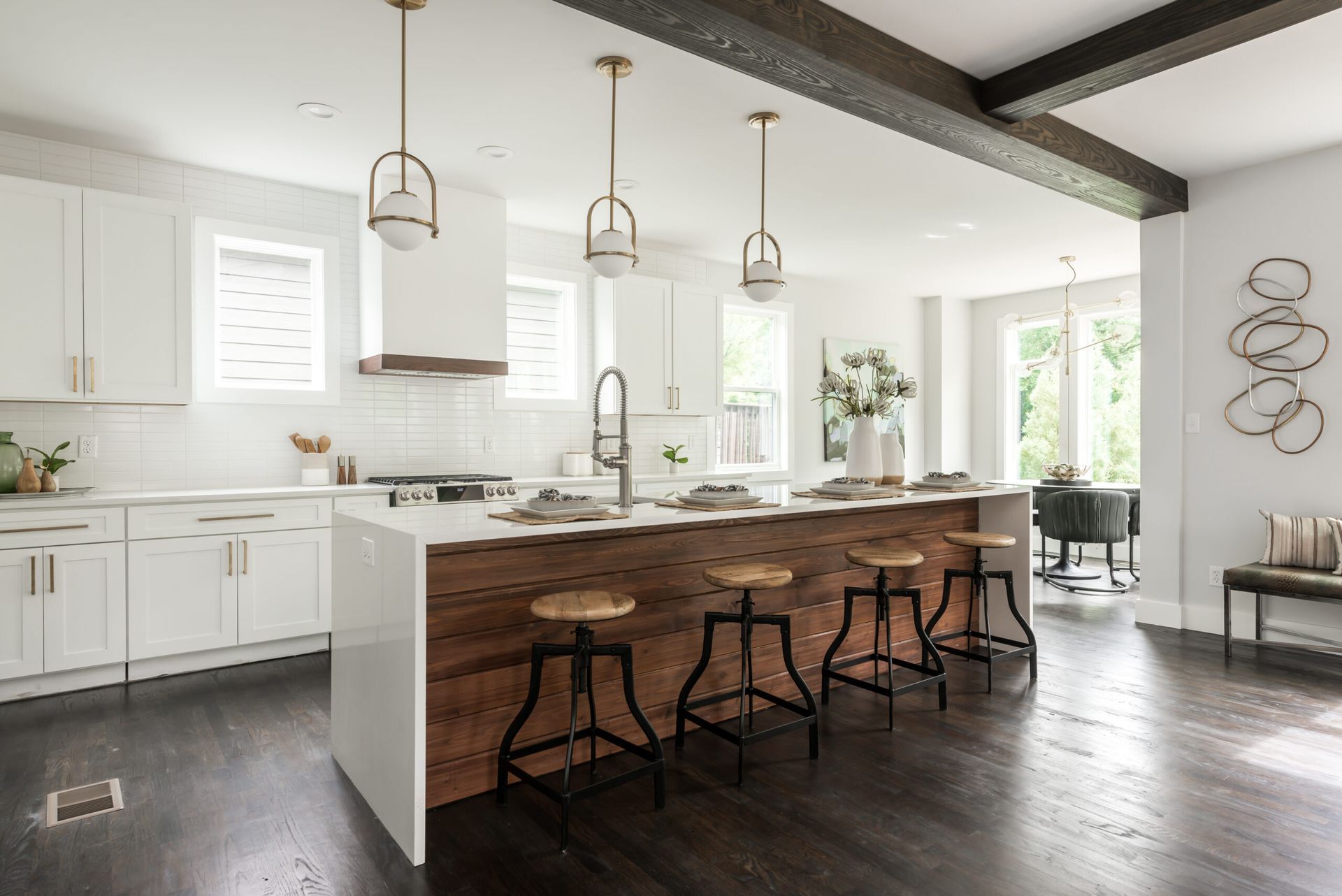 Bright modern kitchen with white cabinets, dark wood island, pendant lights, and bar stools