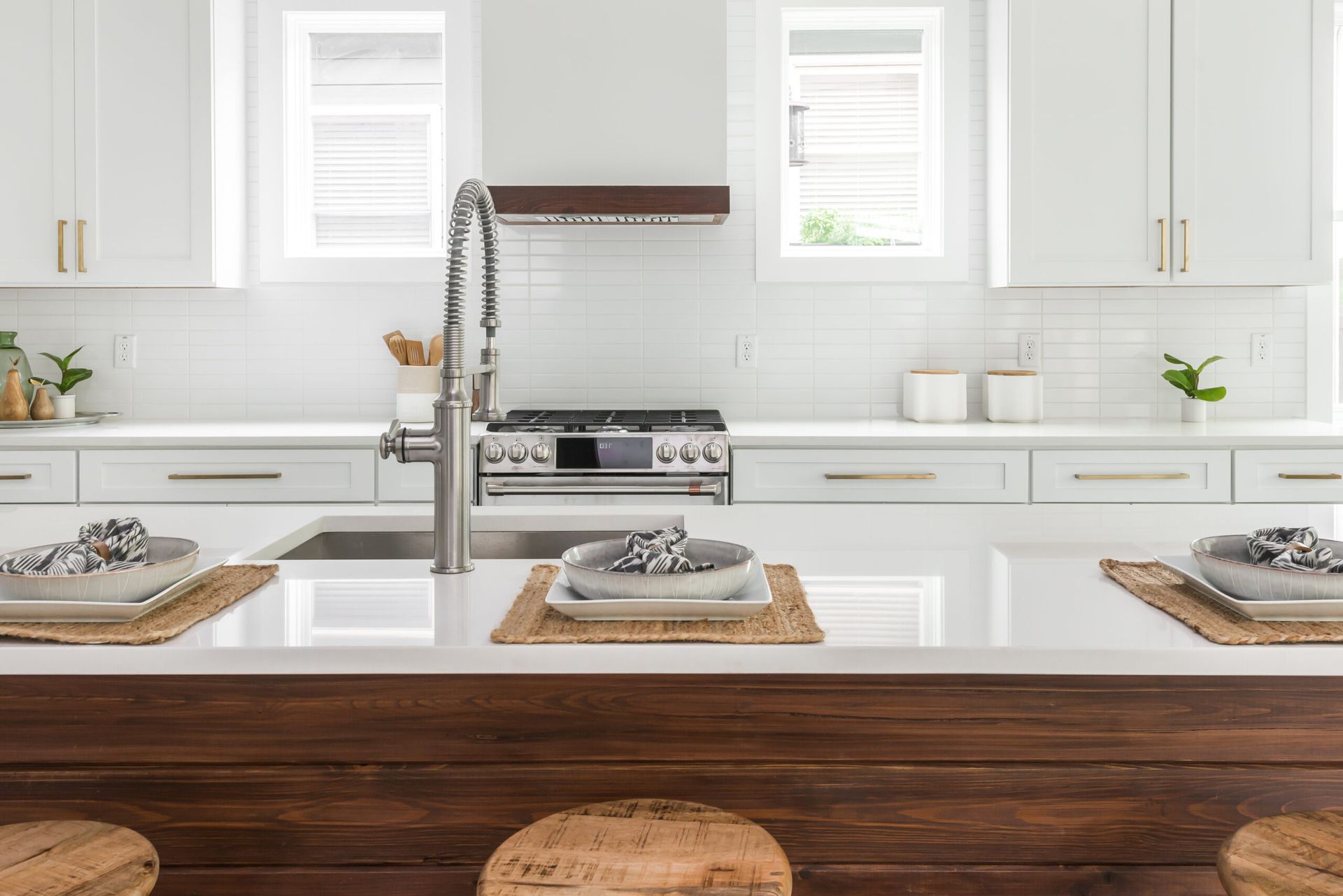Bright white modern kitchen with a wooden island, chrome faucet, and place settings at the counter.