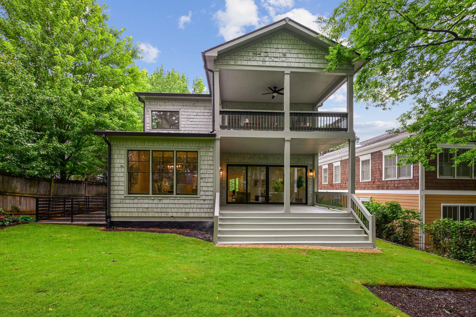 Two-story house with a covered front porch, green lawn, and trees in front
