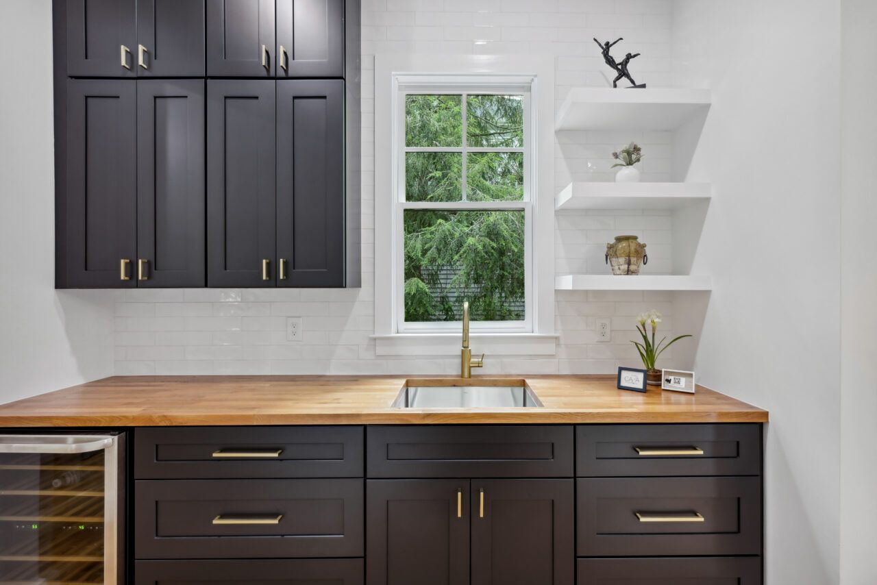 Modern kitchen with dark cabinets, wood countertop, window, and white wall shelves