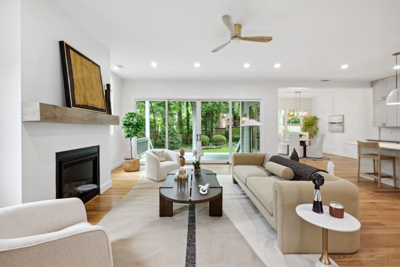 Bright modern living room with fireplace, beige sofas, coffee table, and sliding glass doors to greenery