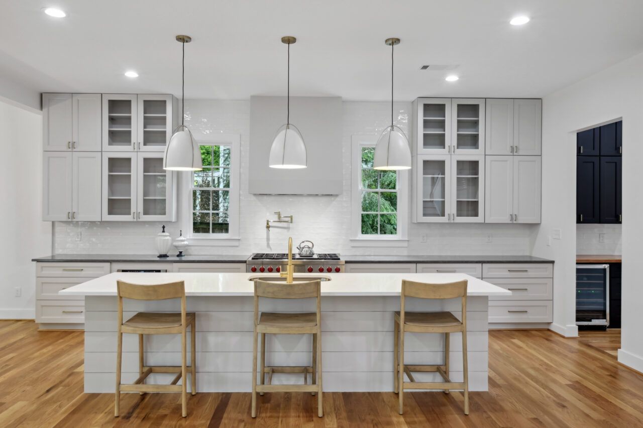 Modern white kitchen with island, wooden stools, pendant lights, and hardwood floors