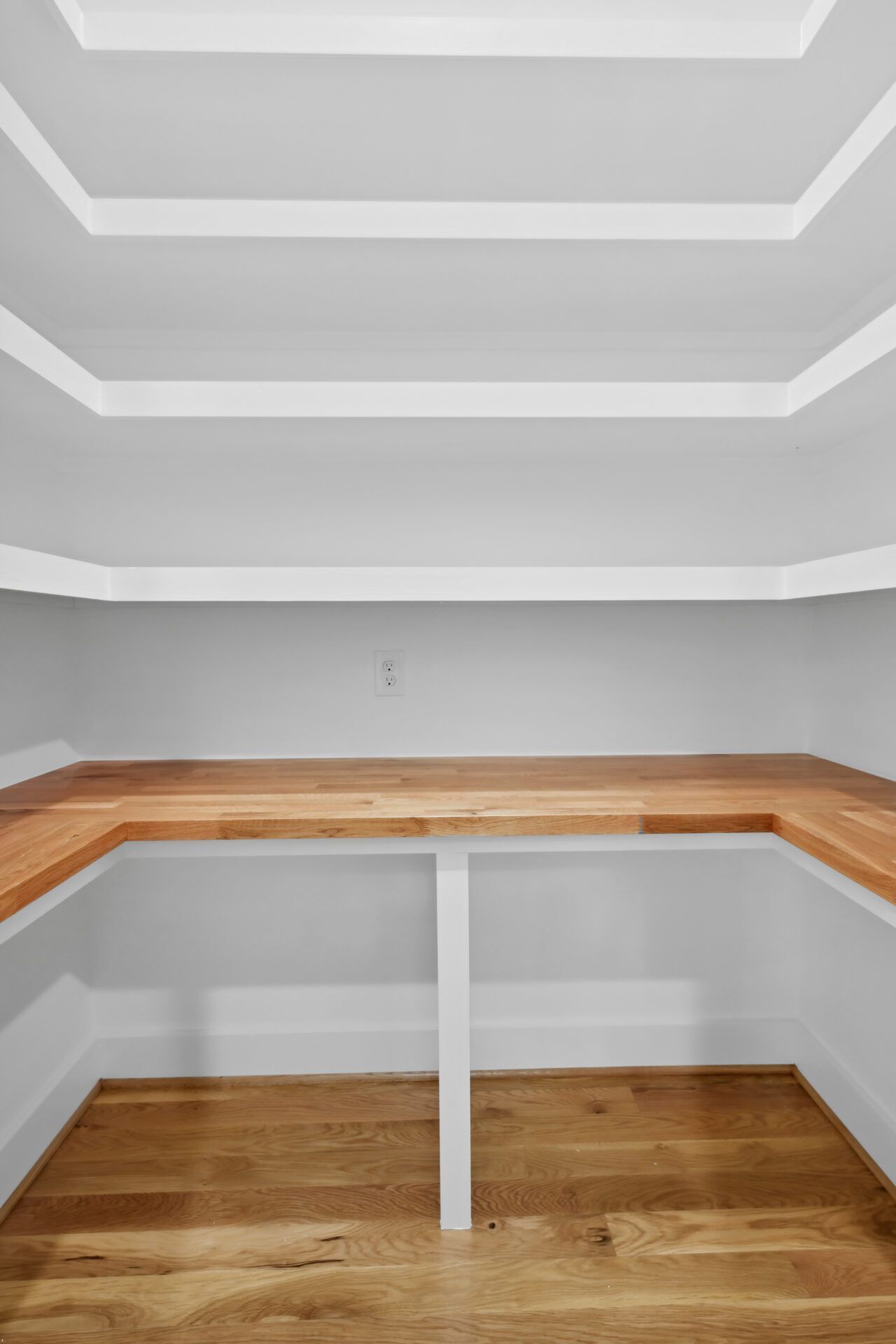 Empty walk-in closet with built-in wooden shelves and hardwood floor, white walls and coffered ceiling.
