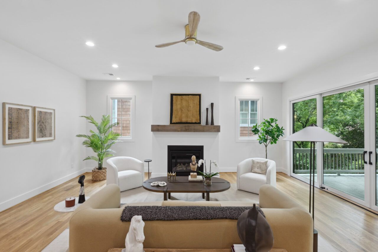 Bright modern living room with white walls, beige sofas, fireplace, ceiling fan, and large sliding glass doors