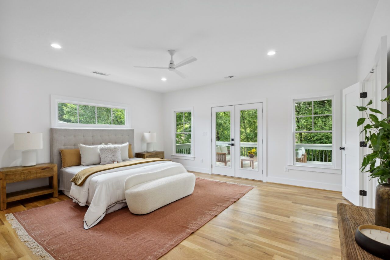 Bright bedroom with bed, rug, wood floors, and large windows overlooking greenery
