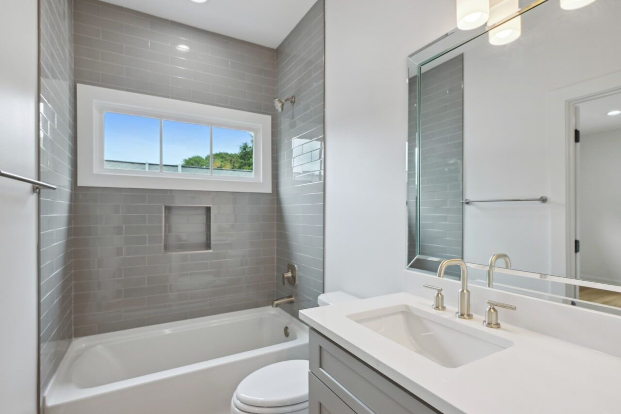 Bright modern bathroom with tiled shower-tub, window, vanity sink, and large mirror