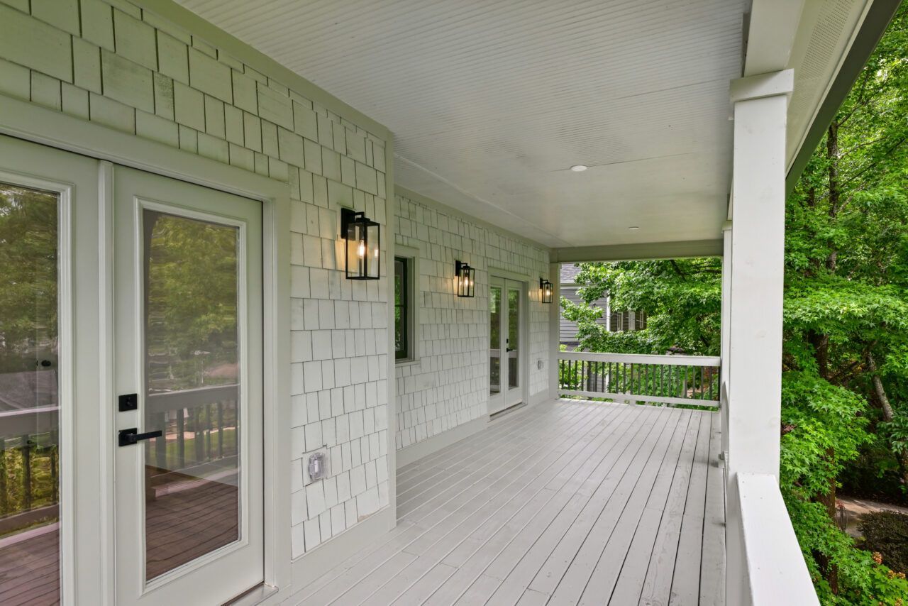 Covered white porch with double doors, black lanterns, and green trees beyond the railing