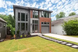 Modern two-story house with tall windows, brick facade, garage, and a green lawn under a blue sky