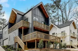 Modern gray and white multi-story townhomes with wooden balconies and stairs on a wooded hillside