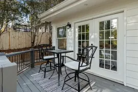 Patio with black metal table and chairs outside a white house with French doors